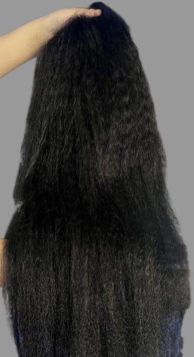 A person holding up a long, dark, curly wig against a solid gray background.