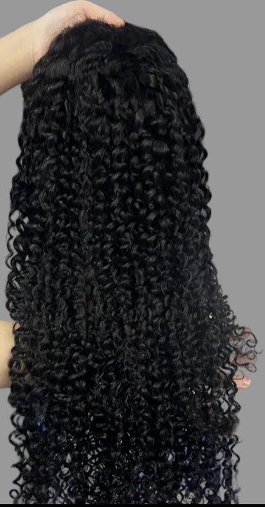 A long, black, curly wig held up by a hand against a solid gray background.