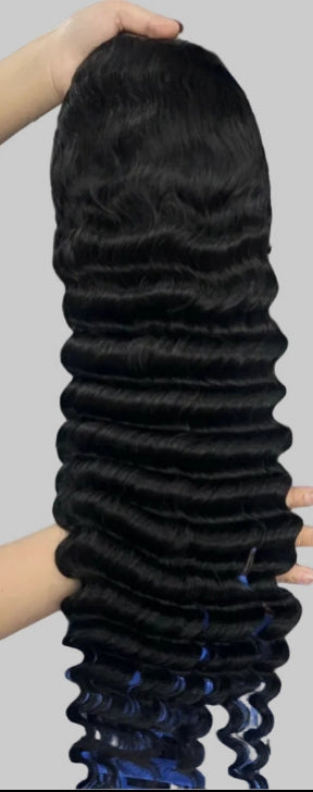 A long, straight black wig with deep wave curls, held up by a person's hands against a plain light gray background.