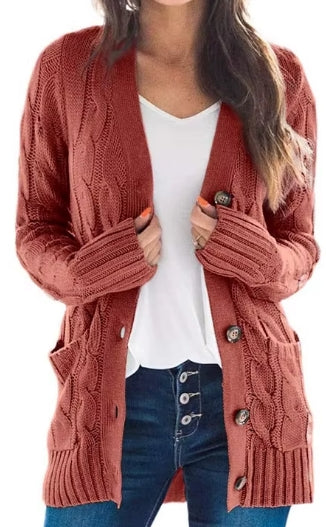 A woman wearing a rust-colored cable-knit cardigan with front buttons and pockets, layered over a white top and blue jeans, shown against a plain white background.