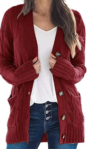 A woman wearing a burgundy cable-knit cardigan with front pockets over a white top and blue jeans, shown from the neck down on a plain white background.