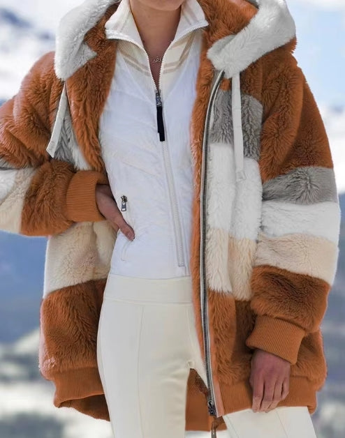 A person wearing a chunky faux-fur striped jacket in warm brown, cream, and light gray, layered over a white zip-front top and white pants, with a snowy outdoor background.