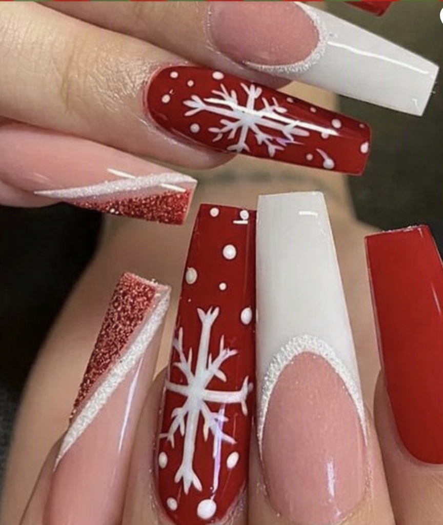 A close-up of a hand showcasing coffin-shaped false nails with a festive holiday design. The nails feature a mix of solid red, white French tips, glittery red, and red with white snowflake patterns.
