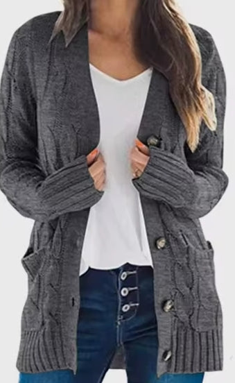 A woman wearing a dark gray cable-knit cardigan over a white top and blue jeans, shown from the neck down against a plain white background.