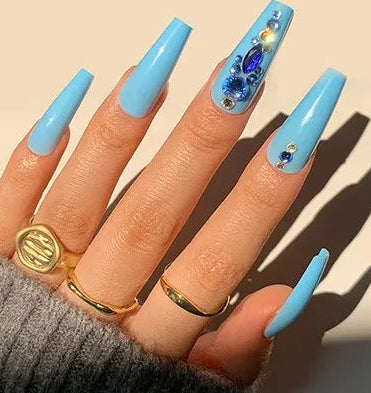A hand wearing long light blue press-on nails with one nail decorated in blue and gold glitter, shown alongside a small inset of the nail set pieces and the text '# 1328'.