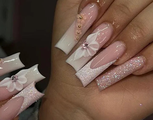 A collage showing a hand with long pink and white coffin-shaped nails decorated with floral designs, glitter, and small gold rhinestones, alongside a sheet of matching nail stickers labeled #2932.