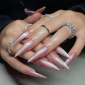 Close-up of a hand with pink stiletto nails and multiple rings on a blurred background