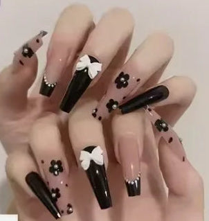 A hand displaying long coffin-shaped press-on nails with a black and nude pink floral design, alongside a small inset showing the full set of nails and the text '#JP1200'.