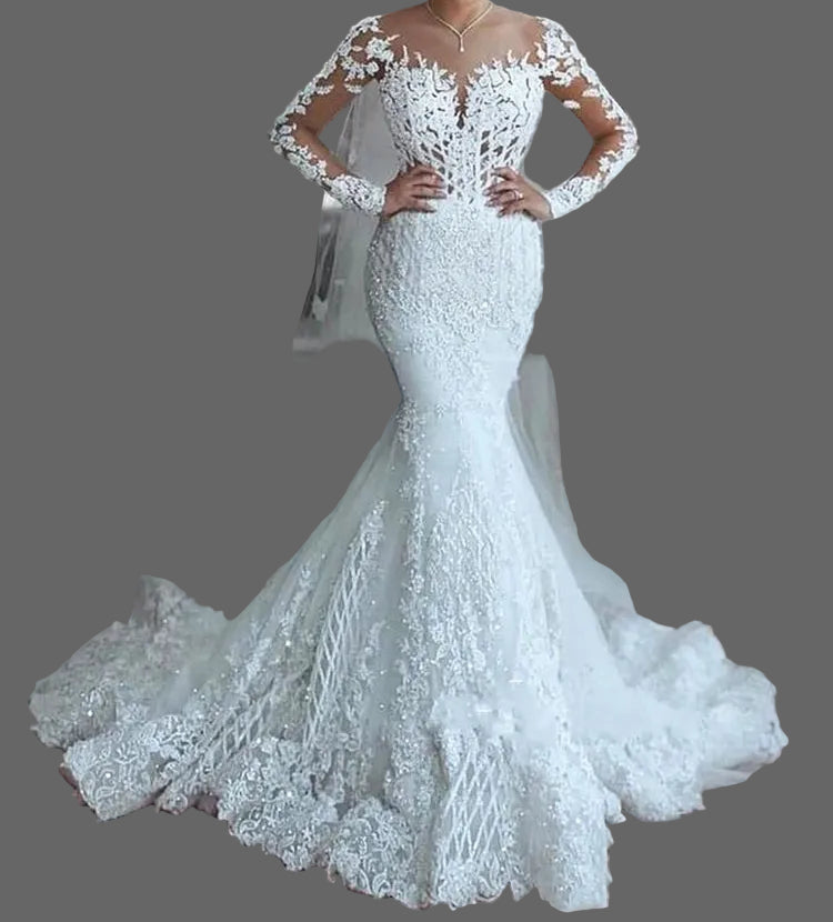 Woman in a white lace wedding dress with a long train and tiara, standing outdoors.