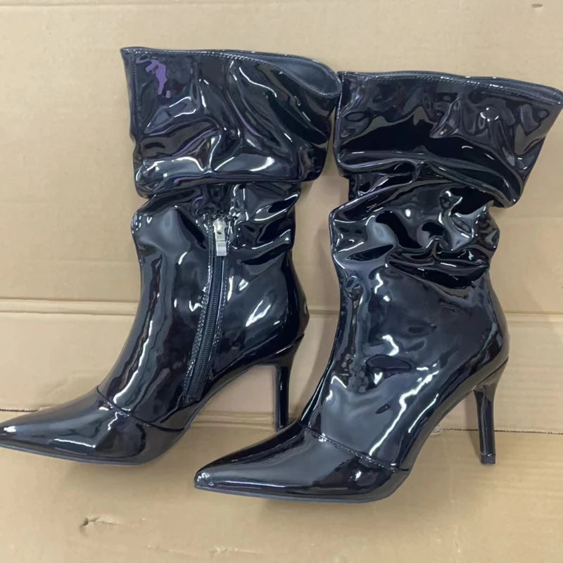 Pair of black patent leather high-heeled boots on a beige background
