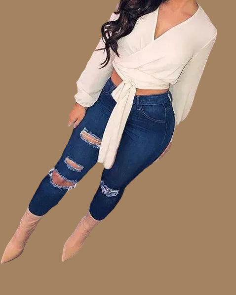 Women's dark blue ripped knee denim leggings styled with a white wrap crop top, front angle view
