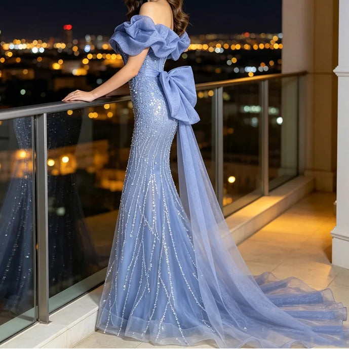 Light blue sequined mermaid evening gown with oversized bow and cathedral train, model on rooftop balcony at night

