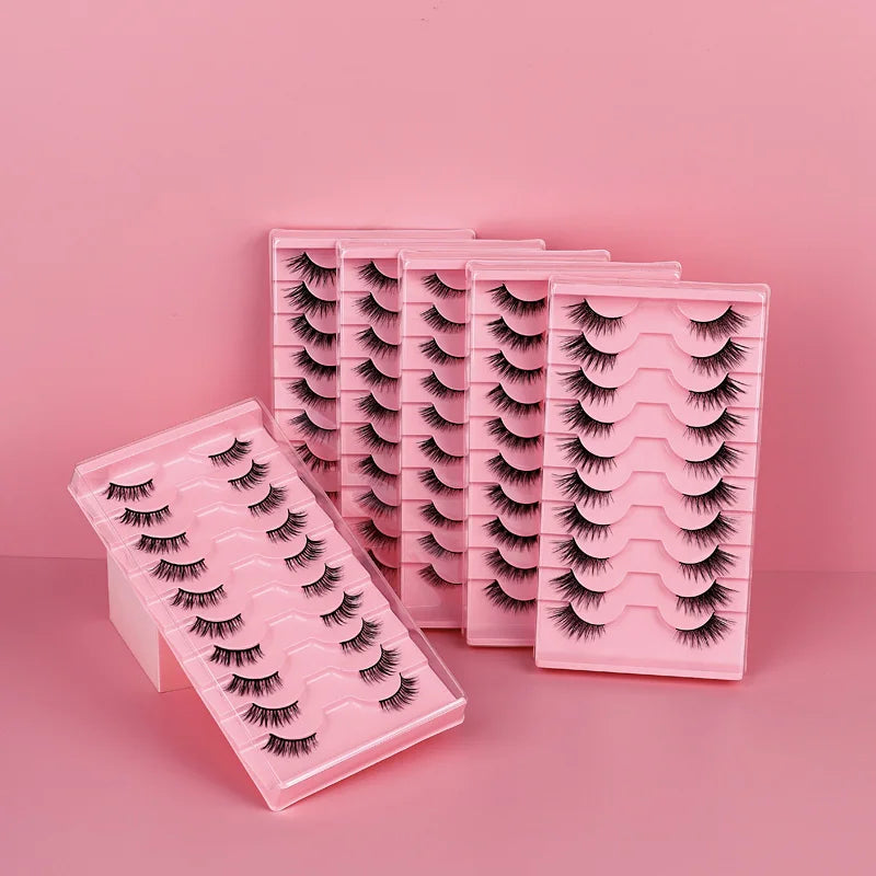 Six pink trays of false eyelashes arranged on a pink background, with one tray open in the foreground to show the lash style.