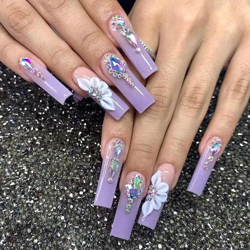 Purple acrylic nails with floral and gemstone decorations on a glittery black background