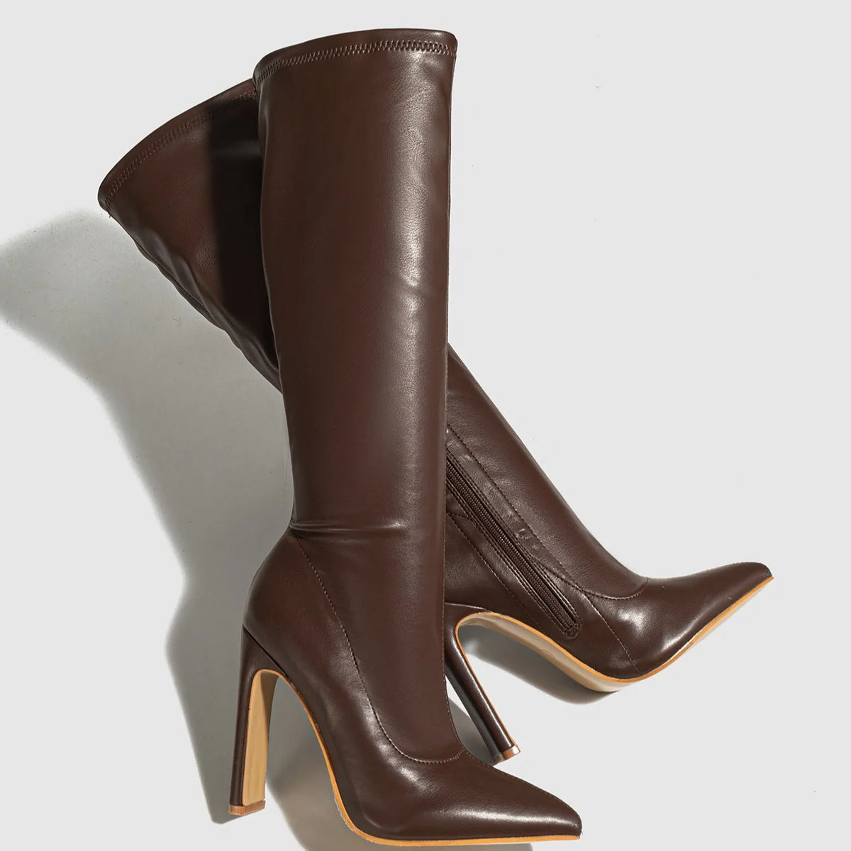 Brown knee-high boots with high heels on a light gray background