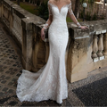  White lace mermaid wedding dress with sheer V-neckline, long floral lace sleeves, and chapel train, front view outdoors

