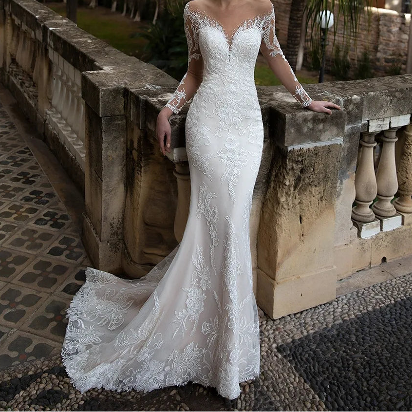  White lace mermaid wedding dress with sheer V-neckline, long floral lace sleeves, and chapel train, front view outdoors

