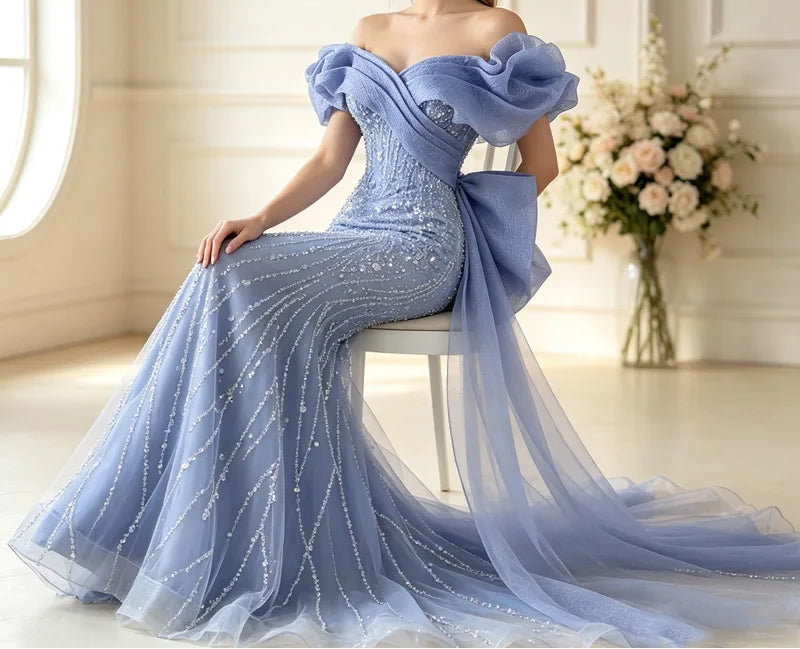 Light blue off-the-shoulder sequined mermaid gown with ruffled sleeves and cathedral train, model seated in elegant room

