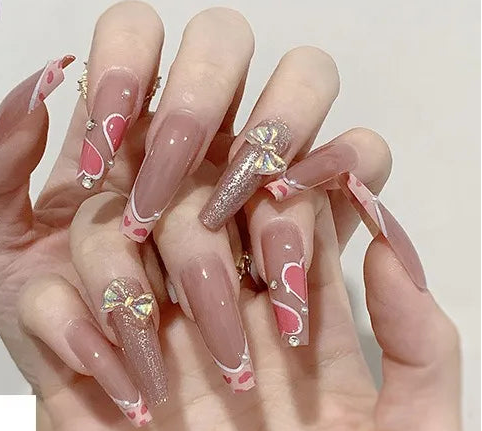 A hand displaying long coffin-shaped press-on nails with a nude pink base, pink heart designs, white curved lines, and gold glitter accents. The image includes a purple label reading '# 1390' and a small inset showing the individual nail tips.