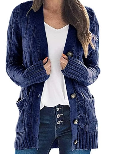 A woman wearing a navy blue cable-knit open-front cardigan with large front pockets and decorative buttons, layered over a white top and dark jeans.