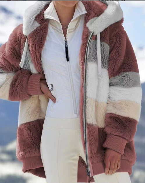 A person wearing a chunky color-blocked fuzzy zip-up jacket with a white zip-front layer and white pants, photographed outdoors against a snowy mountain background.