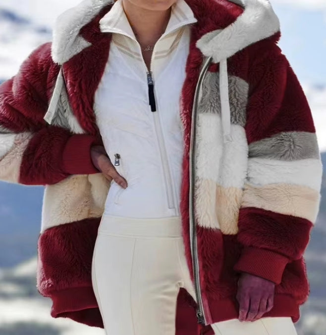 A person wearing a plush faux-fur color-block jacket with deep burgundy, cream, beige, and gray panels over a white zip-front top and cream pants, photographed outdoors against a snowy mountain background.