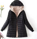 A black quilted puffer jacket with a soft beige sherpa lining, featuring a hood, front zipper, and ribbed cuffs, laid flat against a white background with small decorative props.