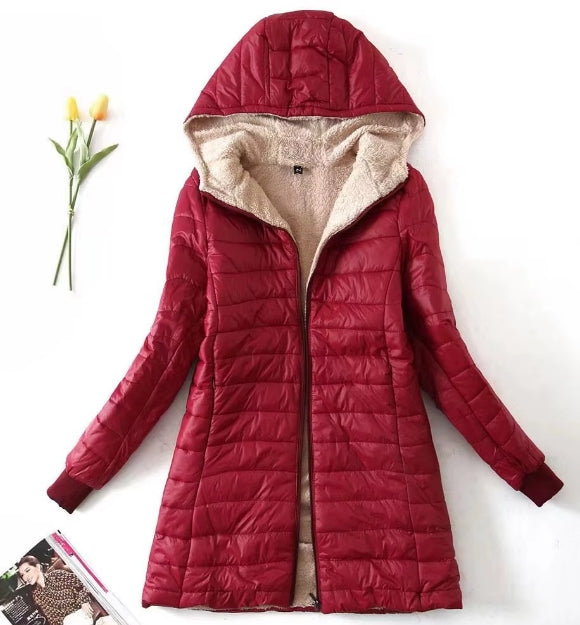 A red hooded puffer jacket with a beige sherpa lining, displayed flat on a white background with a small yellow tulip and a magazine prop.