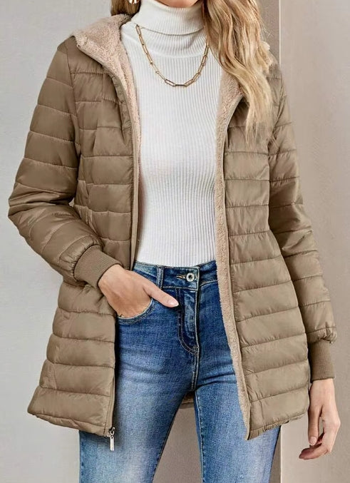 A woman wearing a taupe brown quilted puffer jacket with a beige sherpa-lined hood, layered over a white ribbed turtleneck sweater and blue jeans.
