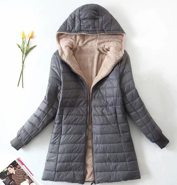 A dark gray hooded puffer jacket with a beige sherpa lining, laid flat on a white background with a small yellow flower and a magazine page as props.
