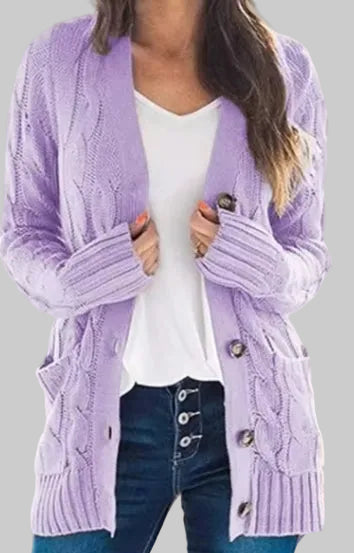 A woman wearing a lavender cable-knit open-front cardigan over a white top and dark blue jeans, shown from the shoulders to the hips in a bright indoor setting.